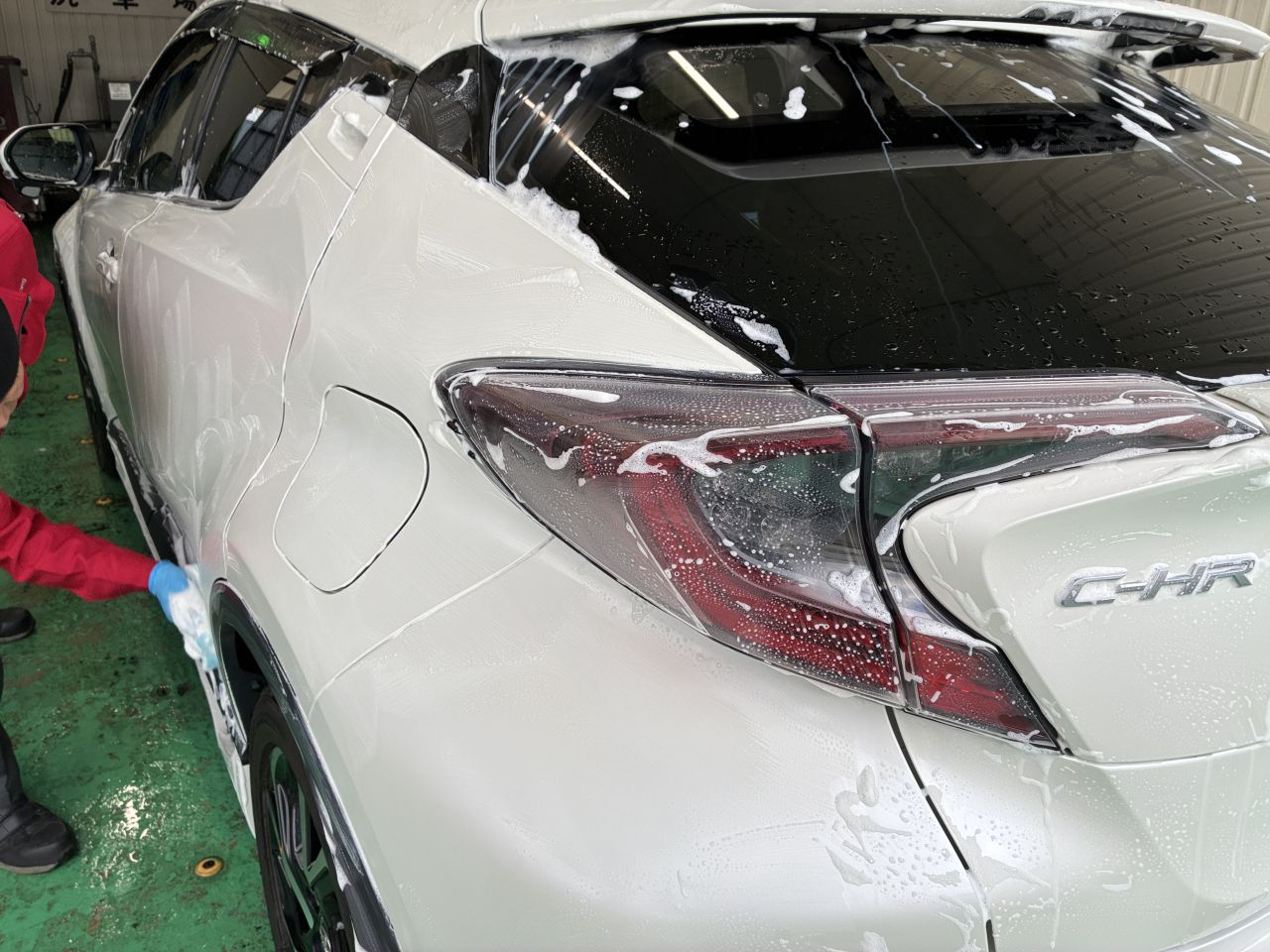 白い車のリア(テールランプ周辺)を、手元で細部まで拭き上げているクローズアップ