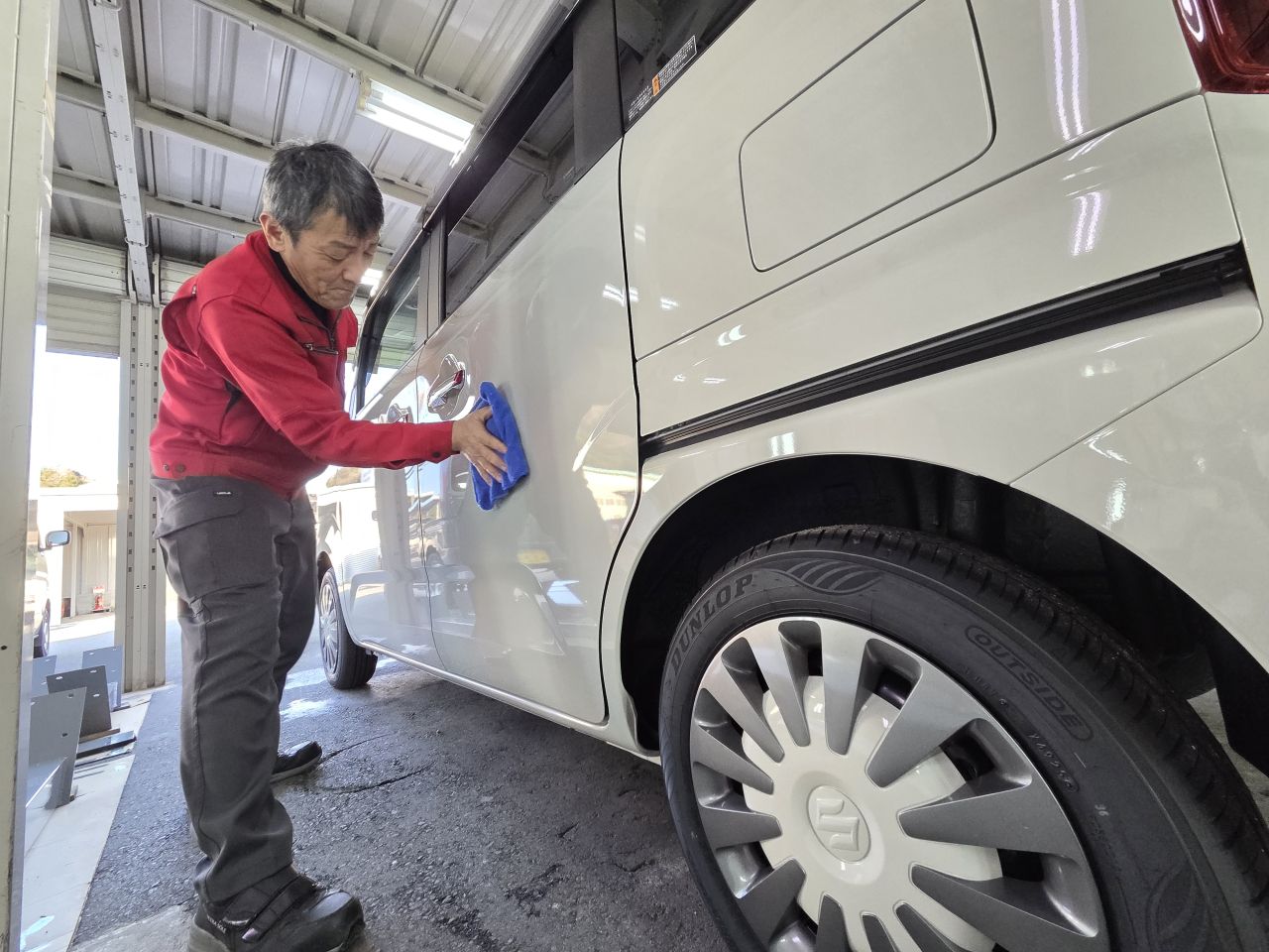 屋内の作業場で、スタッフが白い車のボディ側面をクロスで丁寧に拭き上げている様子