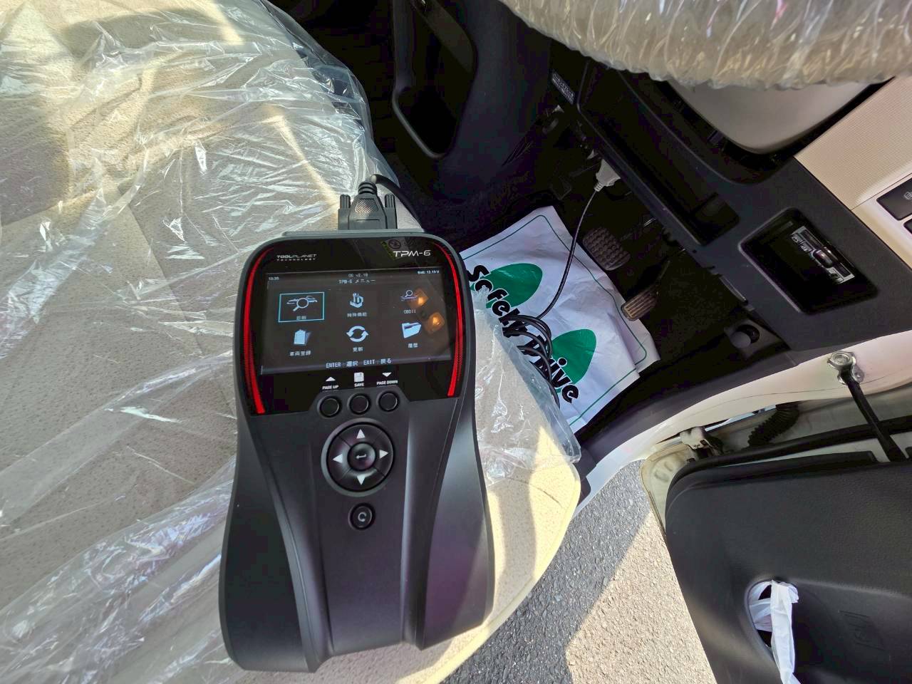 車の運転席付近に設置された、メニュー画面が表示されている黒い自動車用スキャンツール(OBD診断機)