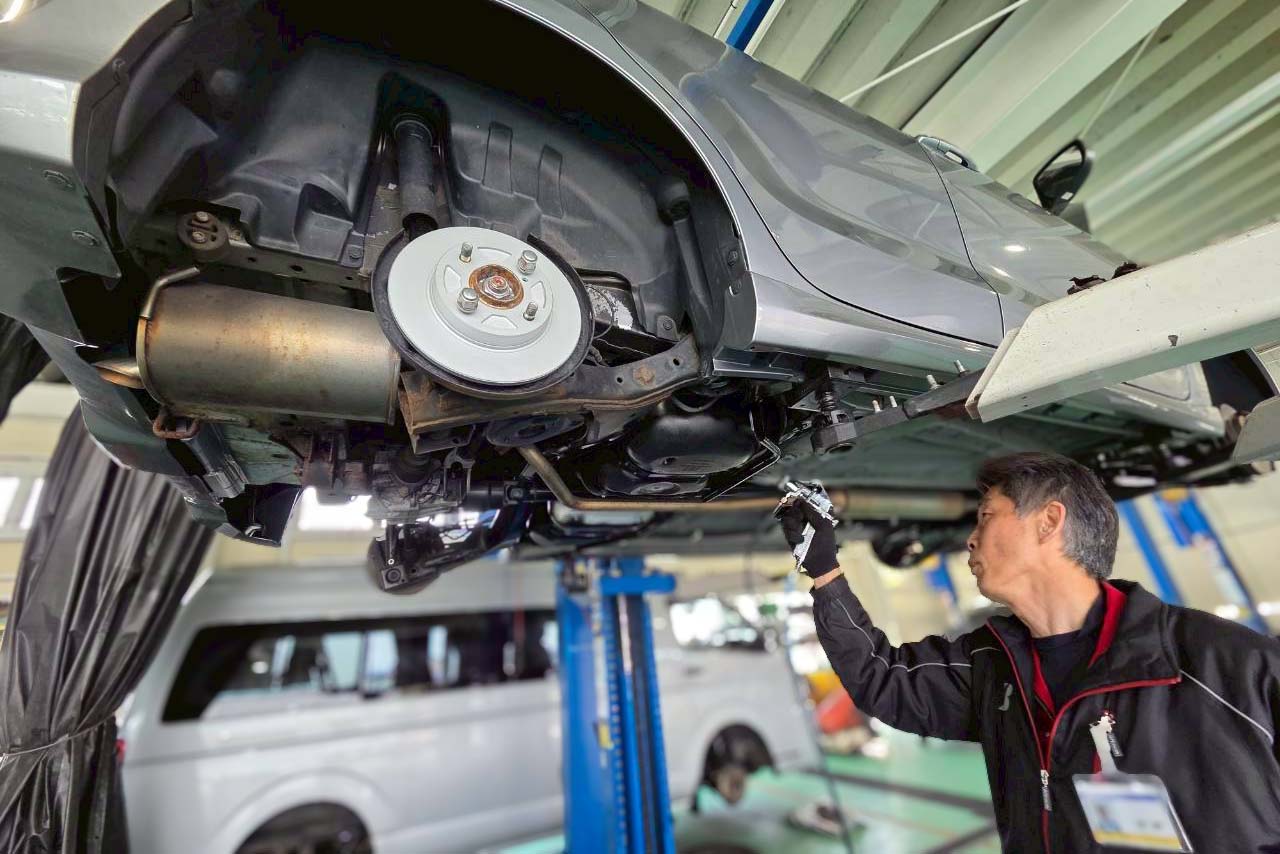 リフトアップされた車両の下回りを真剣な表情で点検する整備士の様子