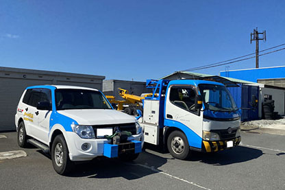 青と白のカラーリングの専用車両と、積載車が屋外に並んでいる様子