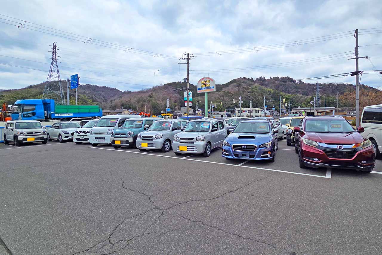 屋外の展示場に整然と並べられた多数の軽自動車や乗用車